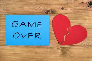 Broken heart and blue paper with text game over on wooden table, relationship breakup concept. photo