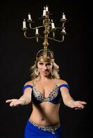 Beautiful belly dancer performing belly dance with candle holder on black background photo