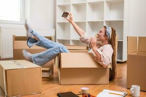 Happy woman having fun and taking selfie with key of her new home while sitting in a box photo