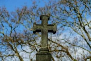 a cross on top of a tombstone in front of trees photo