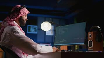 Arab technician writing script code on computer screen inputting commands on terminal. Middle Eastern teleworking employee at home working on fixing company internal database errors video