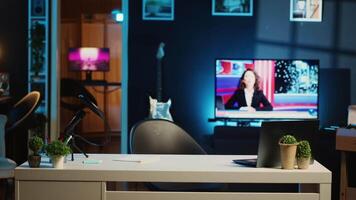 Panning shot of empty home studio interior illuminated with neon lights at night, used for internet video production. Apartment filled with content creation equipment, TV running in background