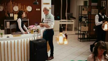 Elderly adult registering in hotel lobby after arriving on international vacation, discussing with front desk staff about room reservation. Concierge offering excellent services to customer. video