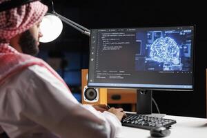 Muslim engineer focuses on a computer screen displaying code and data in a futuristic work setting. He manages a robust cloudbased system while monitoring data on a desktop computer screen. photo