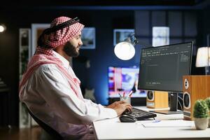 imagen muestra un árabe software desarrollador trabajando a el ordenador personal monitor, sentado a un puesto de trabajo Procesando algoritmo. musulmán descifrador usos un escritorio computadora a trabajo en el usuario interfaz. foto