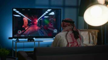 Man playing videogames on TV after long day at work angry after receiging game over screen. Muslim gamer upset after losing at science fiction shooter competition on gaming console video