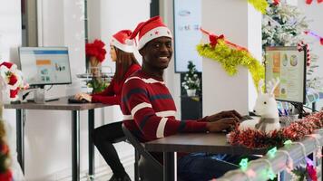 Portrait of friendly african american startup employee working on christmas season in decorated office. Workers solving tasks at workstation in multiethnic workplace during winter festive time photo