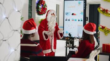 con licencia orador vestido como Papa Noel claus haciendo presentación en frente de empresa trabajadores utilizando caramelo caña puntero. personal aprendizaje cómo a avanzar su carrera durante reunión en Navidad florido oficina foto