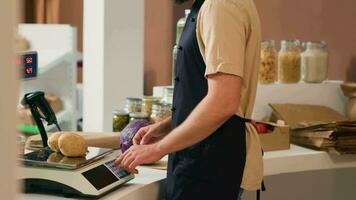 fornecedor ponderação batatas para cliente, vestindo avental às Verificação de saída contador e ajudando cliente para Comprar natural caseiro produzir. lojista usando eletrônico escala para vender Comida dentro reciclável bolsas. video