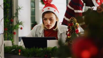 Woman filling paperwork in Christmas decorated office, perturbed by noisy coworkers discussing in background. Employee trying to concentrate on job while colleagues take shift break photo