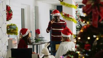 africano americano empleado vistiendo Navidad sombrero entretenido compañeros de trabajo por jugando fingiendo juego durante descanso. colega teniendo divertido haciendo pantomima durante secreto Papa Noel fiesta foto