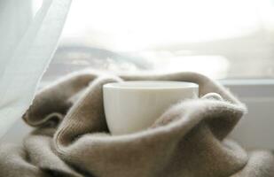 A hot drink on the window on a cold frosty day is on the windowsill next to a cashmere handkerchief on a cold frosty day. High quality photo