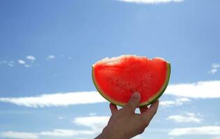 Hand holds a slice of watermelon on a blue sky background. selective focus photo