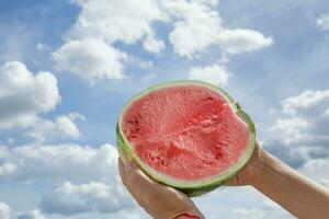 Male hands are holding half of a watermelon against the sky. photo
