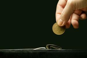 un invisible mujer mano pone un moneda en un billetera.a negro antecedentes foto