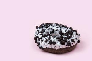 donut in dark chocolate glaze with pieces of chocolate on a pink background. High quality photo