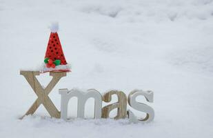 wooden Christmas decoration stands on white snow and Santa red hat on it. selective focus .High quality photo
