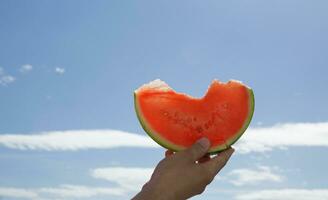 hand holding a slice of watermelon against the blue sky. selective focus photo