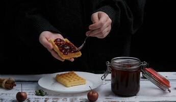 child hands spread strawberry jam with a spoon on Belgian waffles. selective focus photo