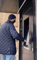 hombre en un negro máscara y un desechable guante usos un Cajero automático. selectivo atención foto