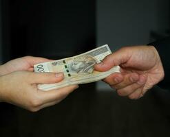male hand giving a bundle of large banknotes to female hands. selective focus photo
