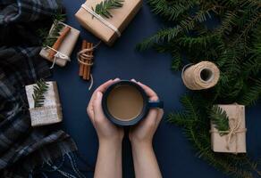 hands hold a cup of coffee over a blue table on which the boxes and scarf lie photo