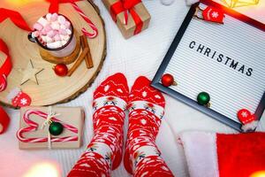 legs in red Christmas socks, letter board and cocoa with marshmallows. next to it lies a gift with sweets and cinnamon sticks . selective focus photo