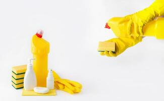 manos en látex guantes sostener un esponja y un botella de desinfectante, y allí son botellas de detergente cercano. selectivo enfocar. blanco antecedentes foto