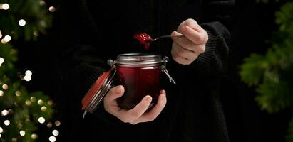 girl holding in her hands jam, cooked at home and near spruce branches with a garland .bokeh.selective focus High quality photo