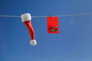 de cerca pequeño Papa Noel claus sombrero y un crédito tarjeta con un imagen colgando en un cuerda en contra el azul cielo. de cerca, alegre Navidad celebracion foto