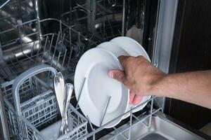 Housework open the dishwasher and the person puts the plate in the machine. High quality photo