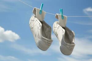 antiguo zapatillas seco en pinzas para la ropa en un cuerda en contra un antecedentes de azul cielo con nubes alto calidad foto