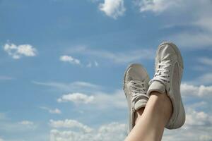 legs in old sneakers on a background of blue sky with clouds. High quality photo