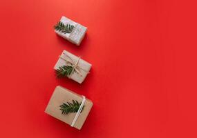 three Christmas gifts lie on a red bright background and the boxes are decorated with spruce branches photo