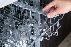 Housework open dishwasher and man putting a glass in the machine. High quality photo