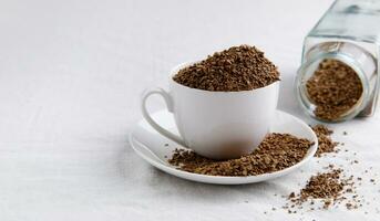 Instant coffee from a glass jar is poured in large quantities into a cup, saucer and tablecloth. High quality photo