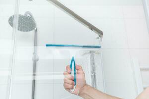 hand with glass scraper cleans glass in shower. High quality photo