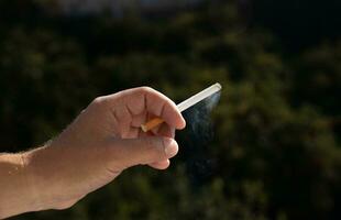 a cigarette in a man's hand against a background of green vegetation. close up. High quality photo