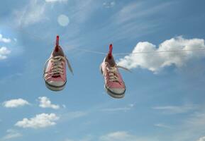 antiguo rosado zapatillas seco en pinzas para la ropa en un cuerda en contra un antecedentes de azul cielo con nubes alto calidad foto