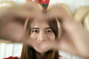 Asian woman making heart with her hands Have fun celebrating Christmas 2024. Decorate and decorate the room with a Christmas tree and 2024 balloons. photo