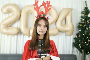 contento asiático mujer celebrando Navidad 2024. decorando y decorando el habitación con Navidad árbol y 2024 globos foto
