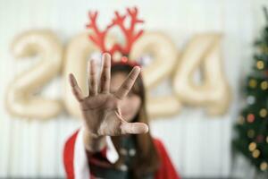 Asian woman raises her hand to stop Celebrating Christmas 2024, the room is decorated and decorated with a Christmas tree and 2024 balloons. photo