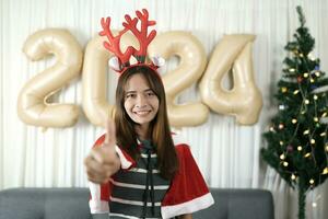 Happy Asian woman celebrating Christmas 2024. Decorating and decorating the room with Christmas tree and 2024 balloons. photo