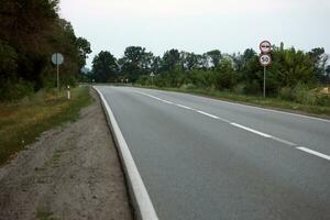 Empty asphalt road and floral field of different grass and flowers in evening time photo