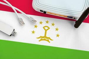 Tajikistan flag depicted on table with internet rj45 cable, wireless usb wifi adapter and router. Internet connection concept photo
