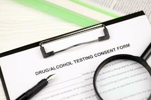 Drug and alcohol testing consent form on A4 tablet lies on office table with pen and magnifying glass photo