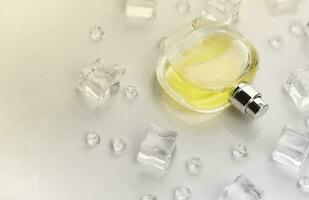 Female perfume yellow bottle, Objective photograph of perfume bottle in ice cubes and water on white table. View from above. Mockup product photo, concept of freshness photo