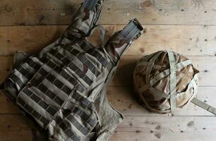 A military helmet of a Ukrainian soldier with a heavy bulletproof vest on wooden table in checkpoint dugout photo