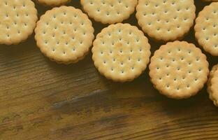 A round sandwich cookie with coconut filling lies in large quantities on a brown wooden surface. Photo of edible treats on a wooden background with copy space