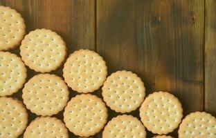 A round sandwich cookie with coconut filling lies in large quantities on a brown wooden surface. Photo of edible treats on a wooden background with copy space